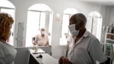 An older patient wearing a mask checking in a with a receptionist