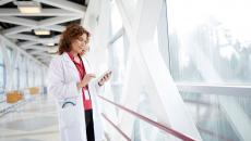 Healthcare provider standing in a hallway looking at a tablet next to a giant window