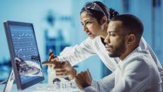 Two healthcare providers sitting in front of a computer touching the screen 