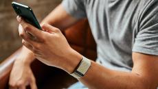 A close up of a man wearing the WHOOP 4.0 on his wrist while using a smartphone